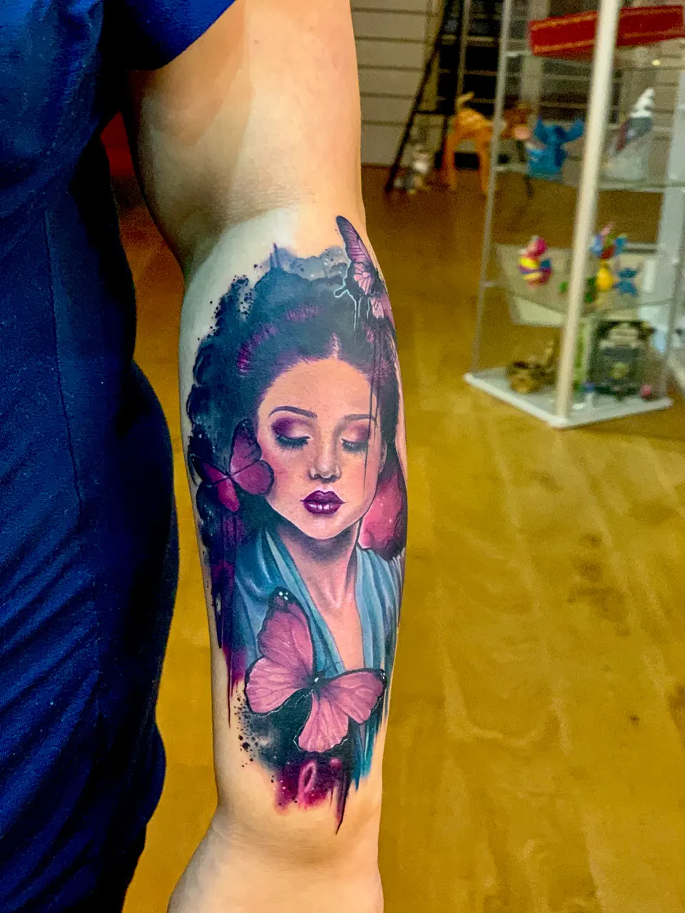 Farbiges Tattoo einer Frau mit Schmetterling in Blau- und Pinktönen