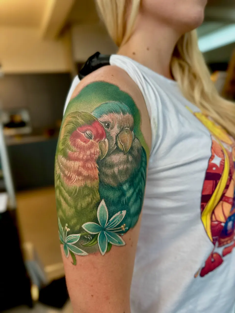 Bunter Papagei mit Blüten als Oberarm-Tattoo